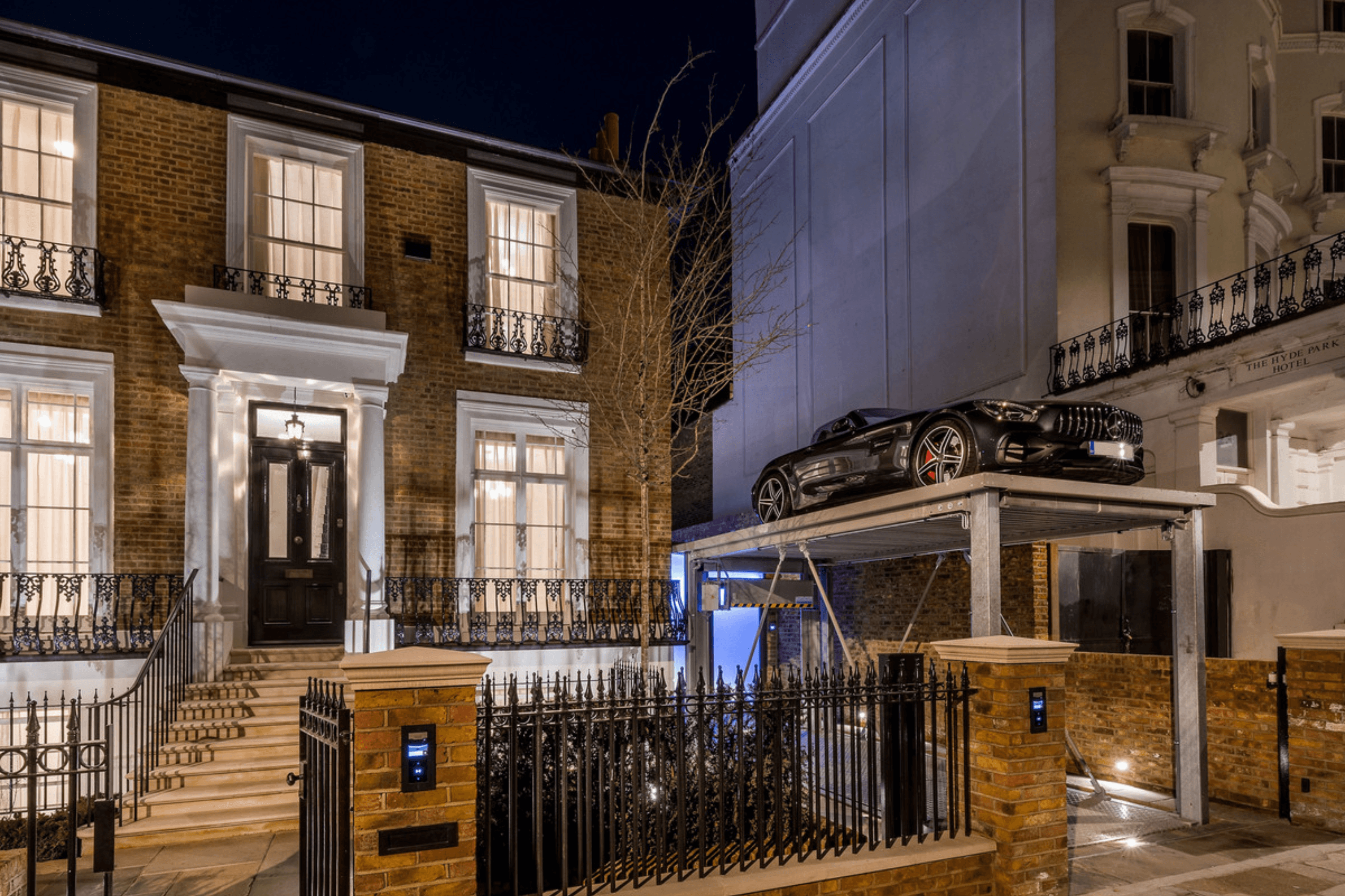 Night time exterior of a double fronted Victorian villa in Notting Hill with off street parking and a car lift platform positioned above the driveway.