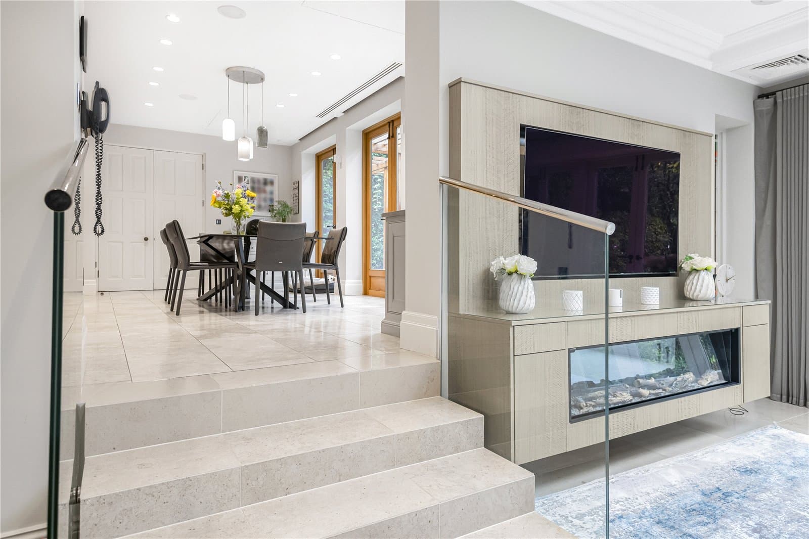 Open plan living and dining area with stone steps, glass fireplace feature wall and large windows overlooking the garden.