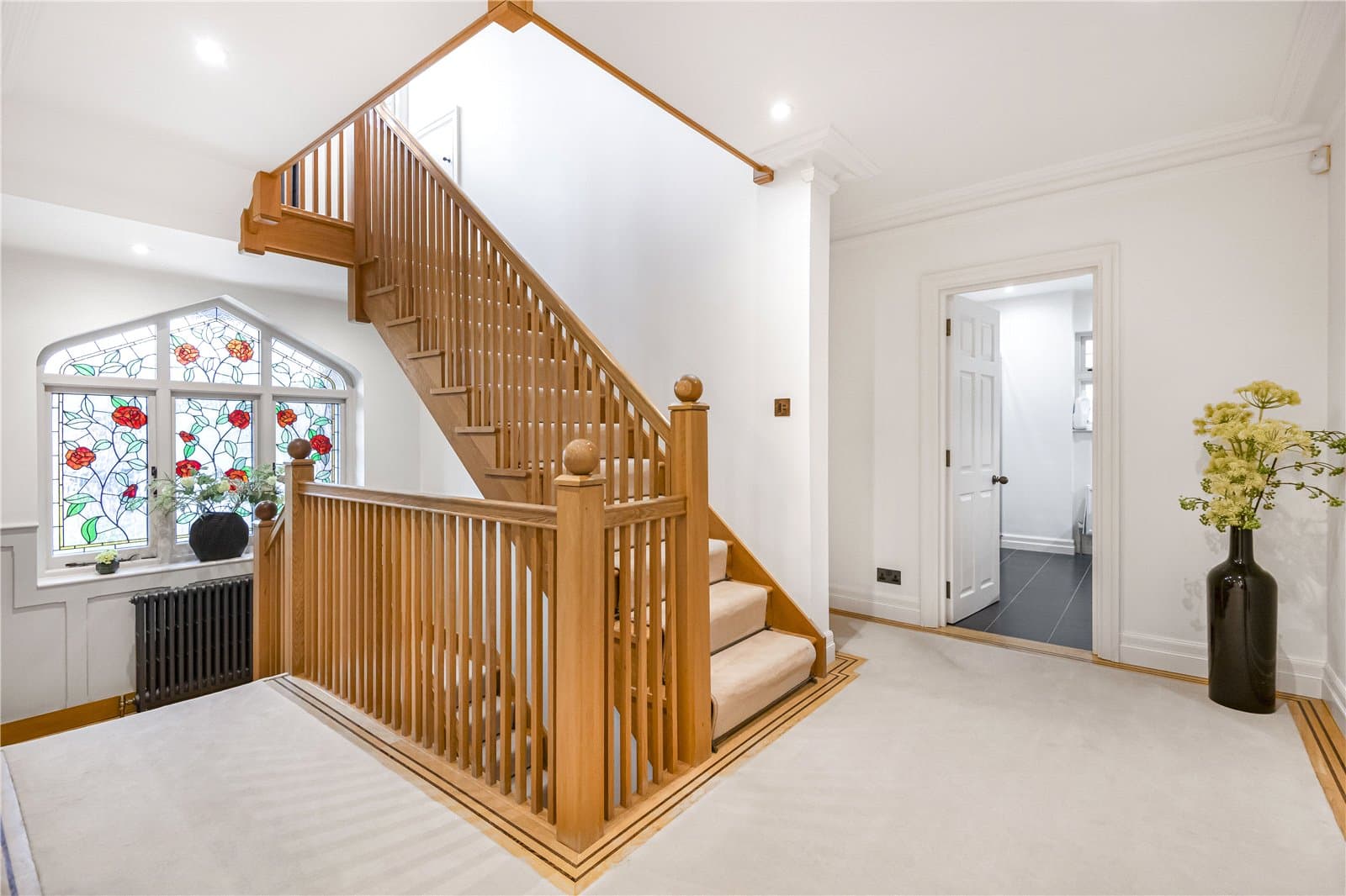 Staircase landing with natural wood balustrade and decorative stained glass window bringing light into the upper hall.