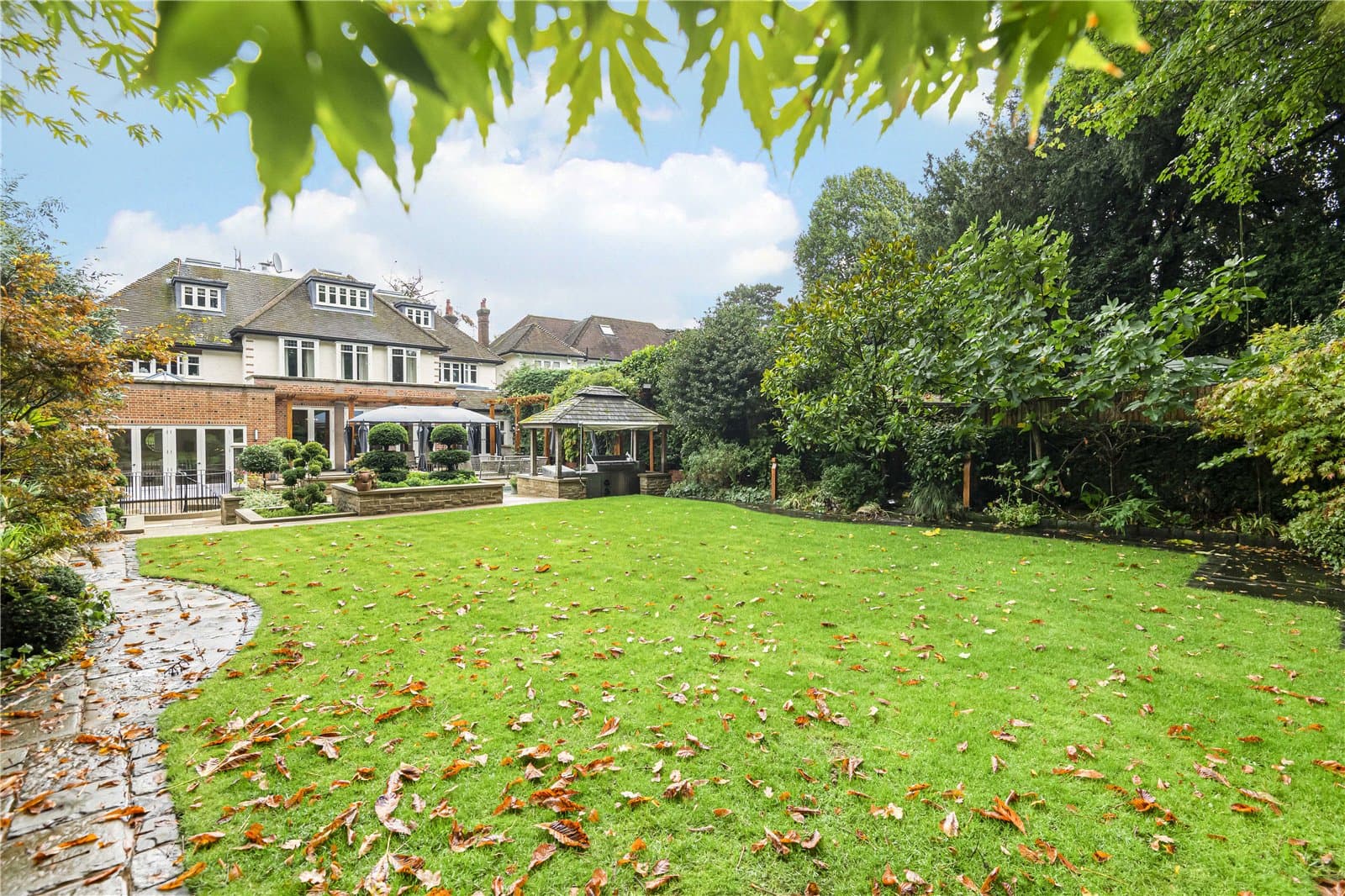 Landscaped rear garden with lawn, mature planting and outdoor entertaining terrace behind the residence.