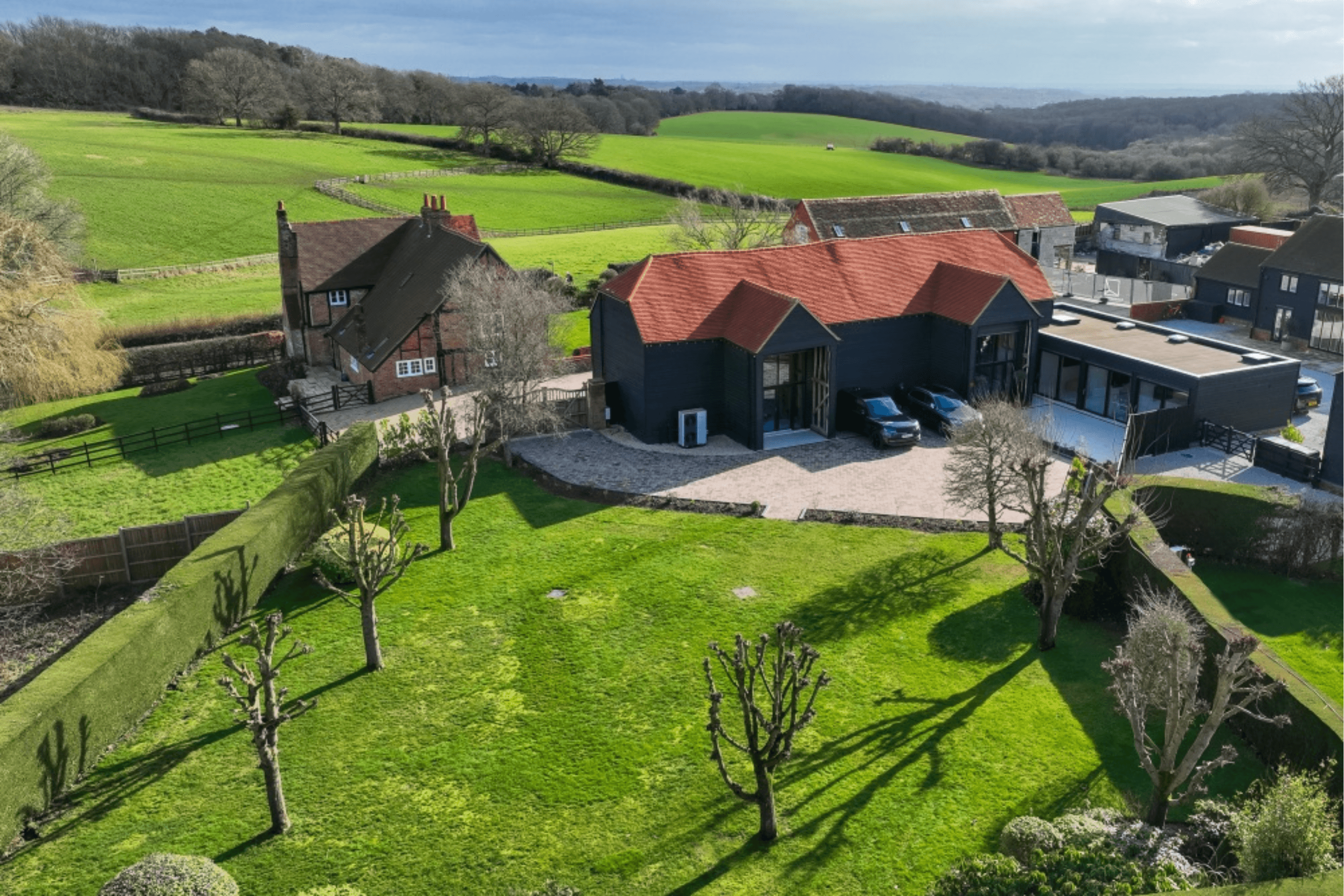 Aerial view of the restored heritage barn at The Bullsland Estate set within landscaped gardens and surrounded by countryside in Chorleywood, Hertfordshire.