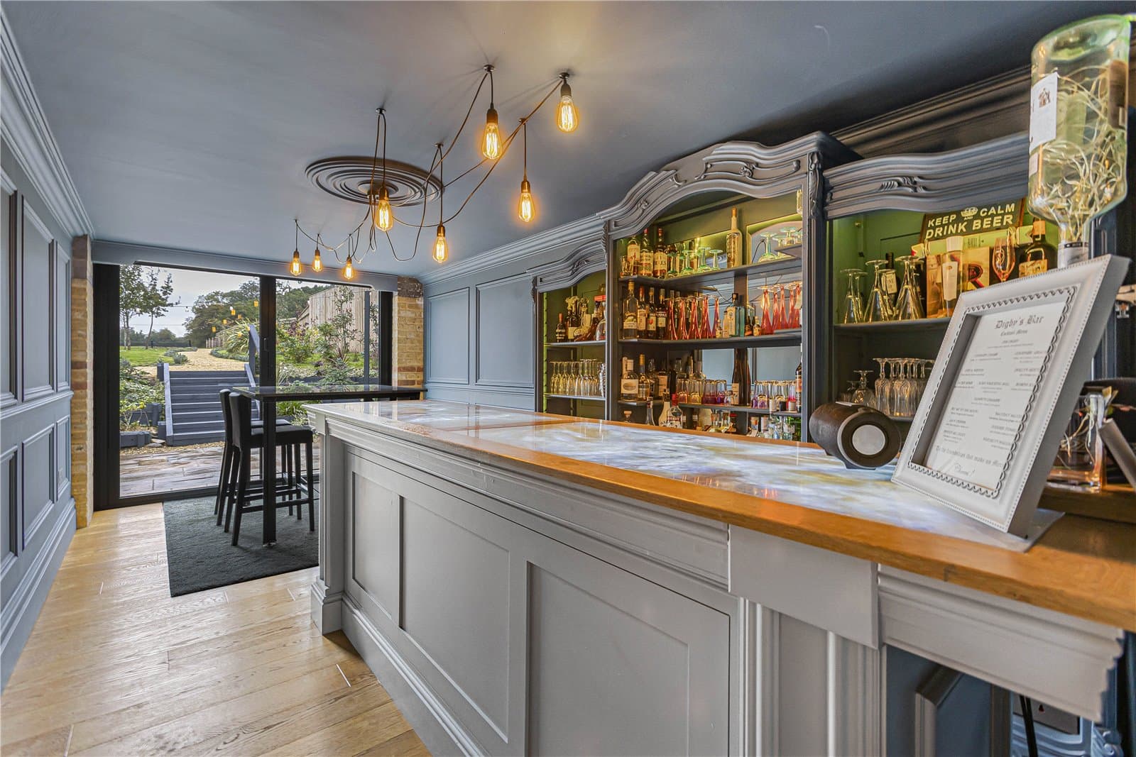 Entertaining room with bespoke cocktail bar, marble counter and garden views through full height glazing