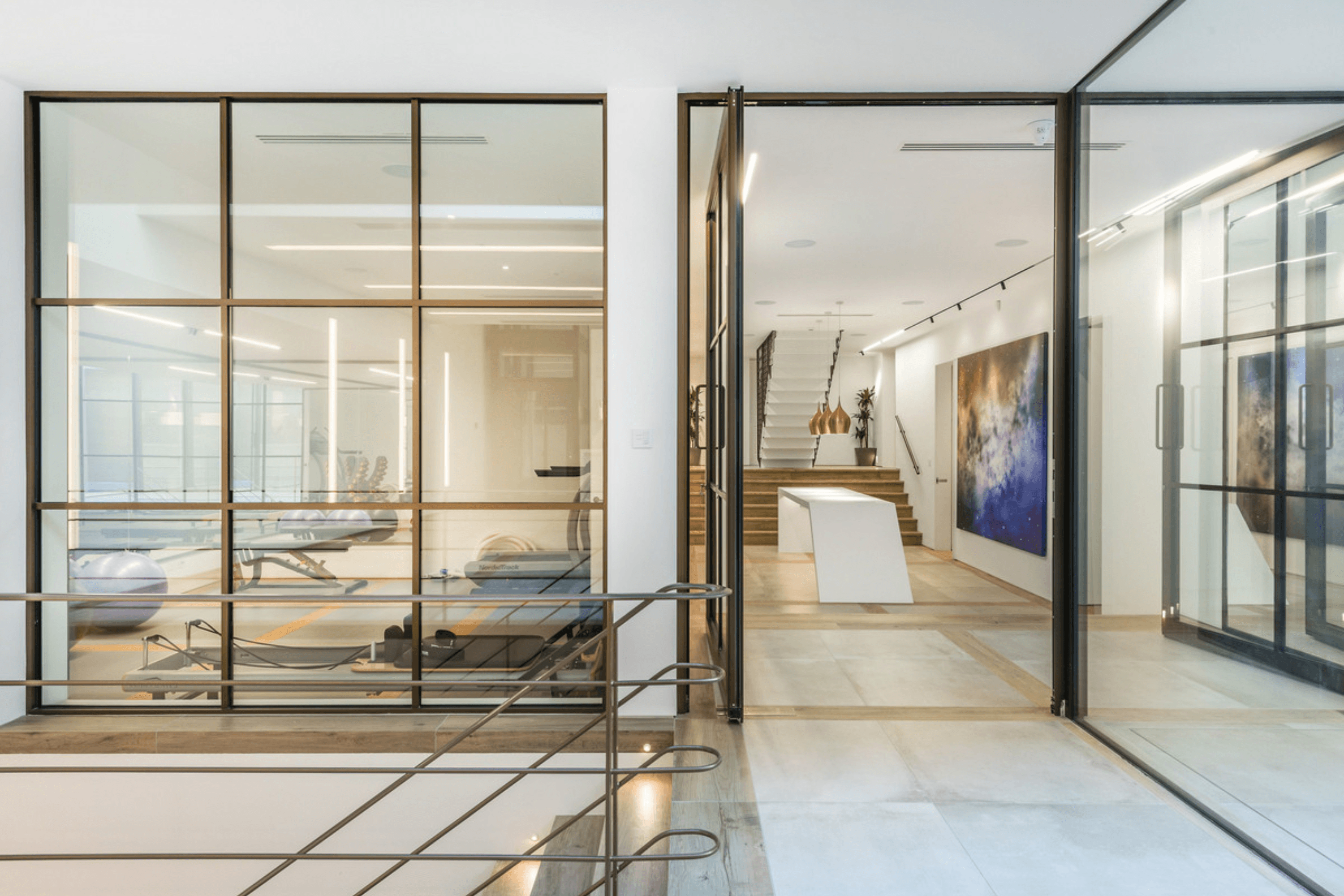 Interior bridge walkway with steel framed glazing overlooking a private gym on the lower level.