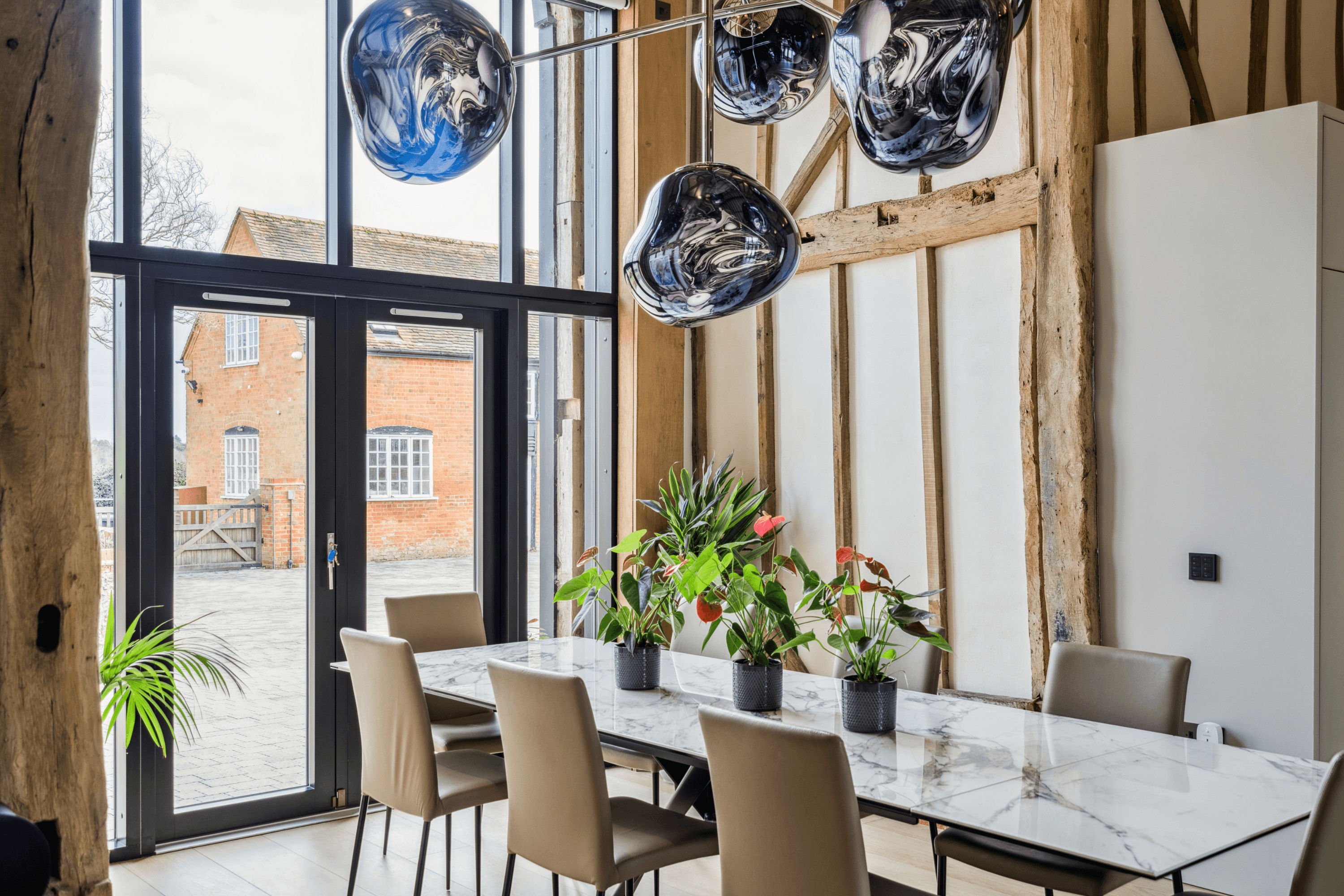 Dining space within the Great Room featuring marble dining table, sculptural pendant lighting and full height glazing overlooking the garden.