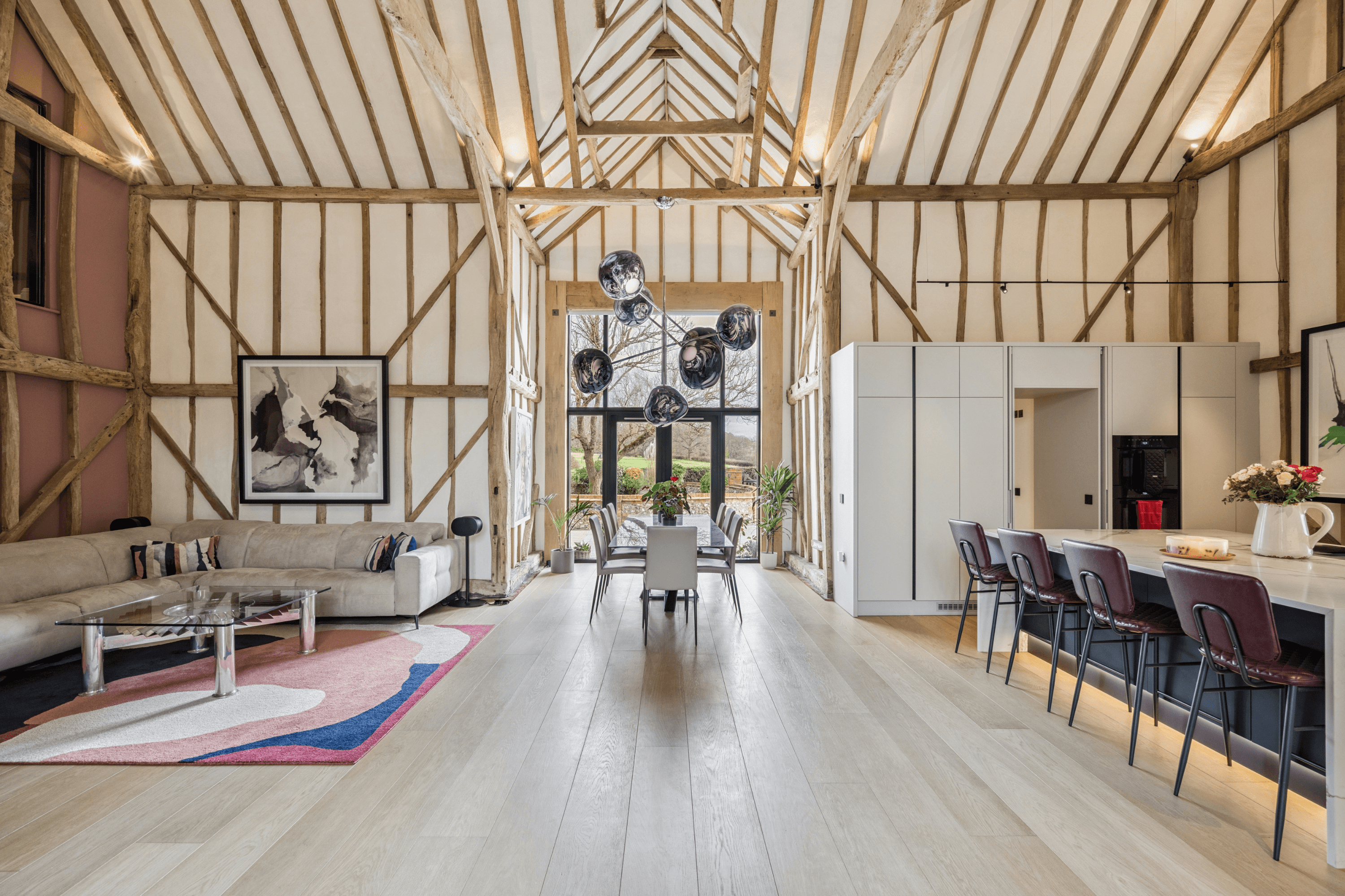 Grand open-plan living and dining space with exposed timber beams, vaulted ceiling and expansive glazing overlooking the gardens.