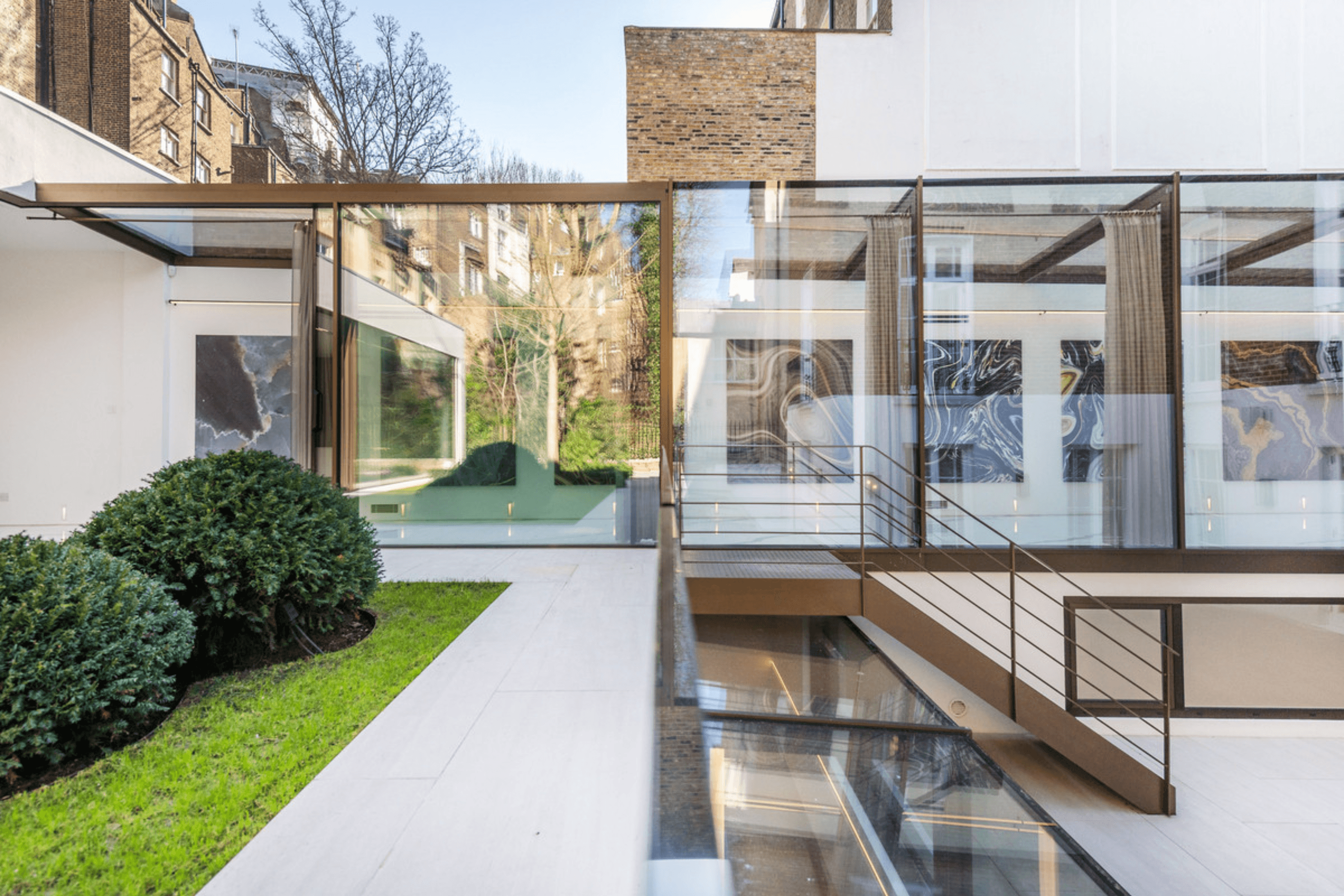 Rear courtyard view of a double fronted Victorian villa with floor to ceiling glazing, landscaped lawn and glass bridge connecting the rear extension.