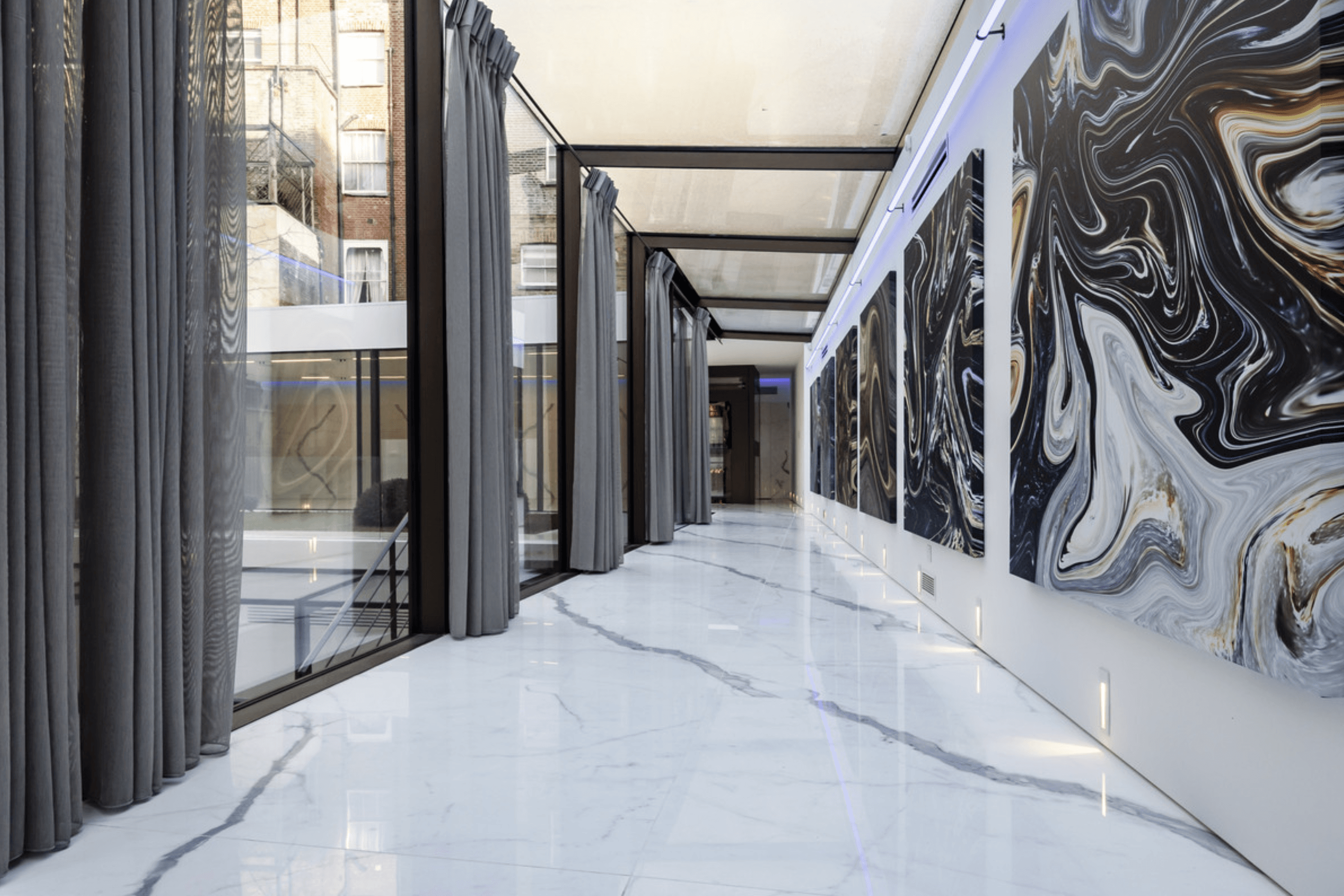 Marble floored gallery corridor with floor to ceiling glazing and large contemporary artworks lining the wall.