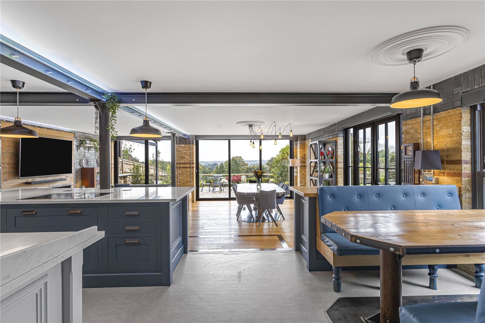 Open plan kitchen and dining space with marble island, exposed brick walls and large sliding doors opening to terrace