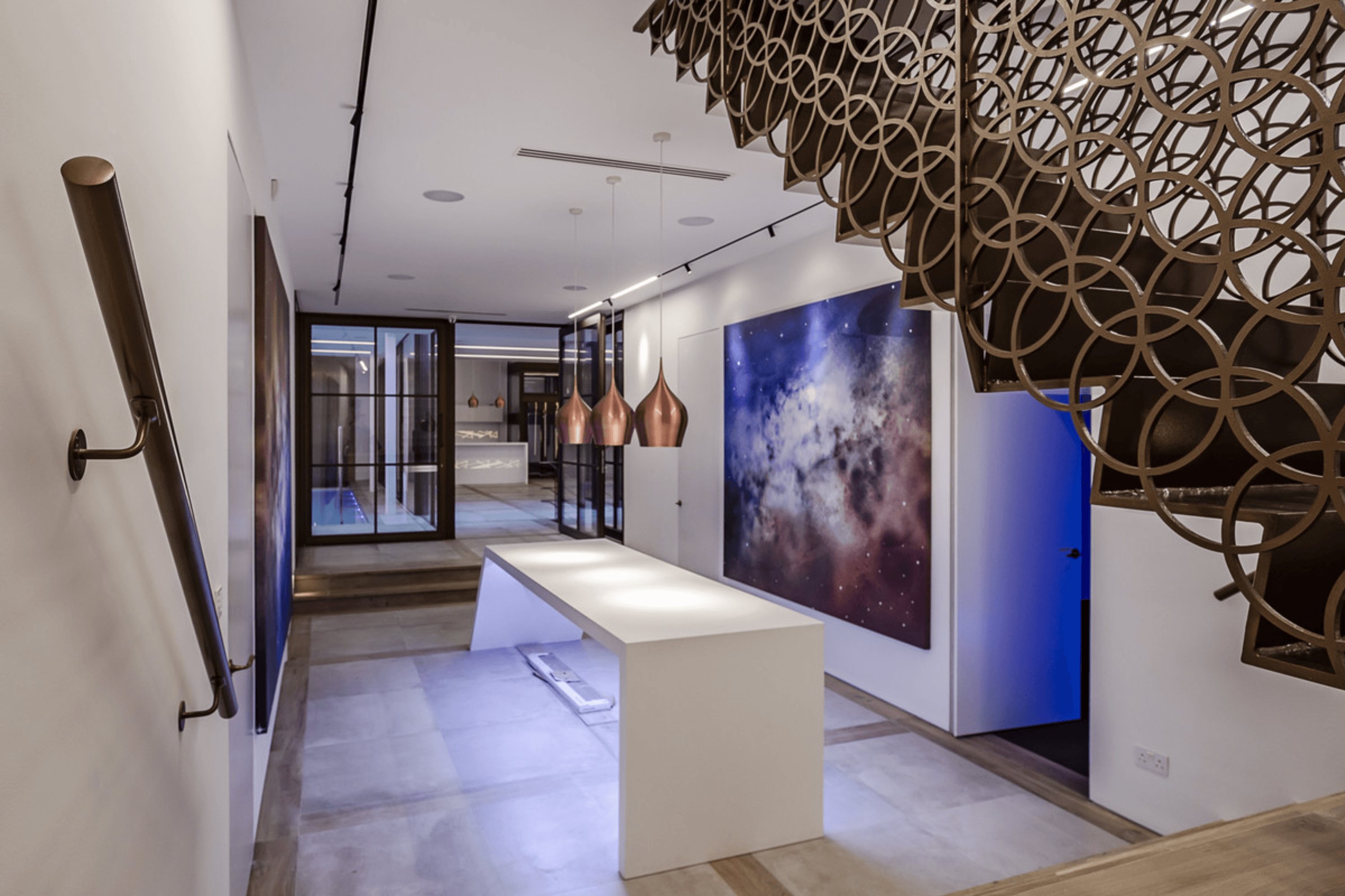 Lower ground hallway with sculptural staircase, pendant lighting and large contemporary artwork leading towards glass framed reception space.