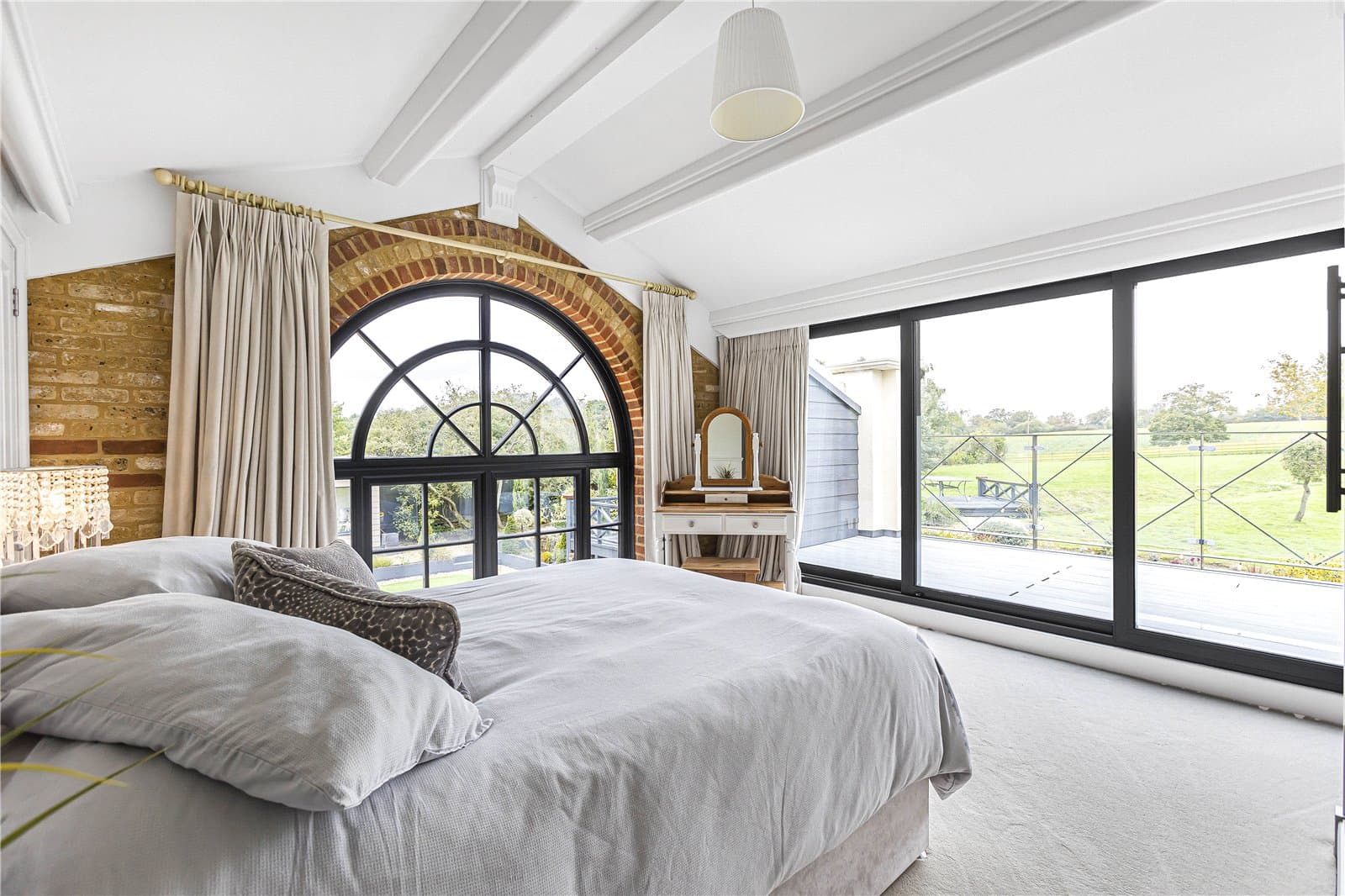 Principal bedroom suite with arched window, exposed brick feature and balcony overlooking the gardens