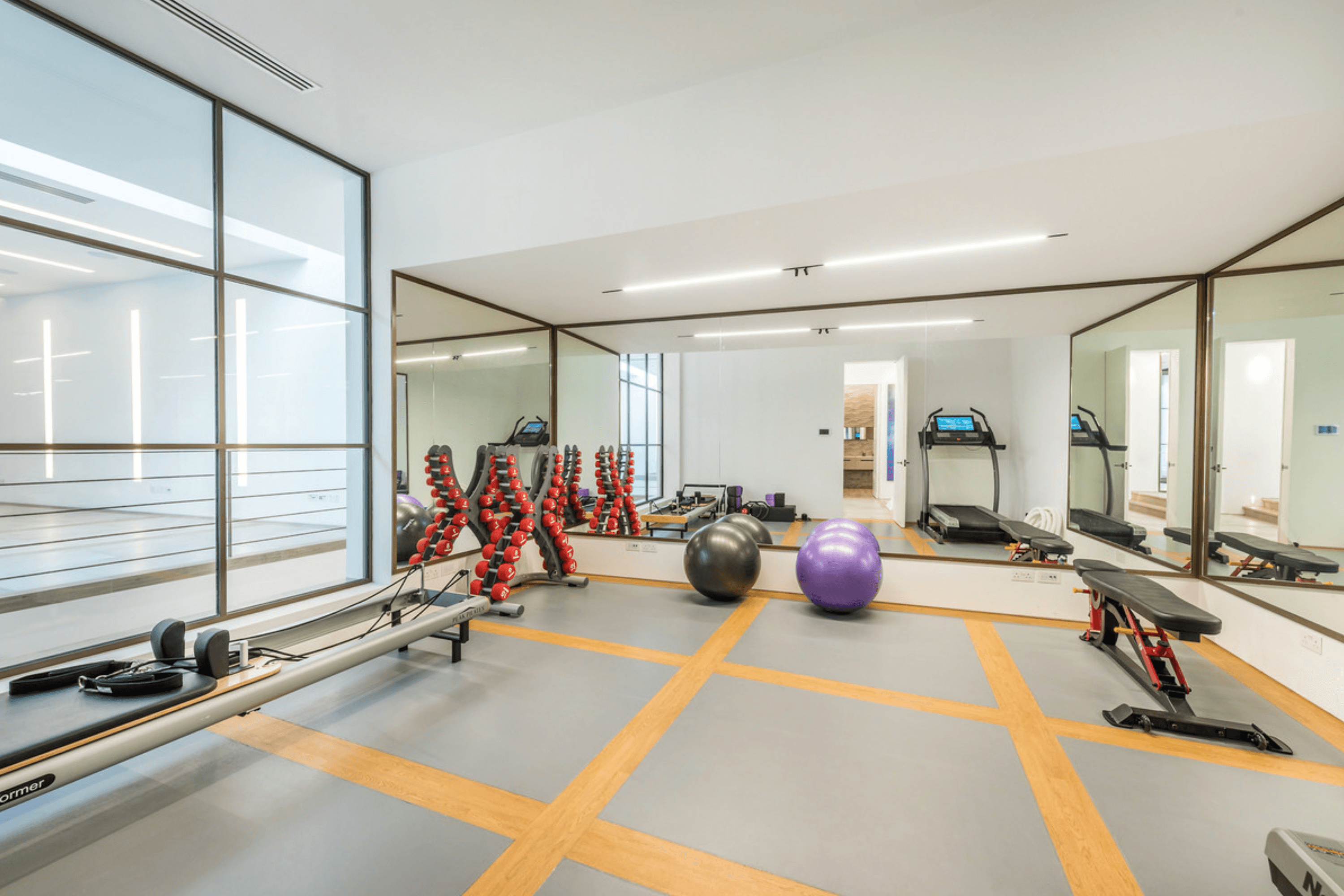Fully equipped gym with mirrored walls, free weights, treadmill and Pilates reformer.