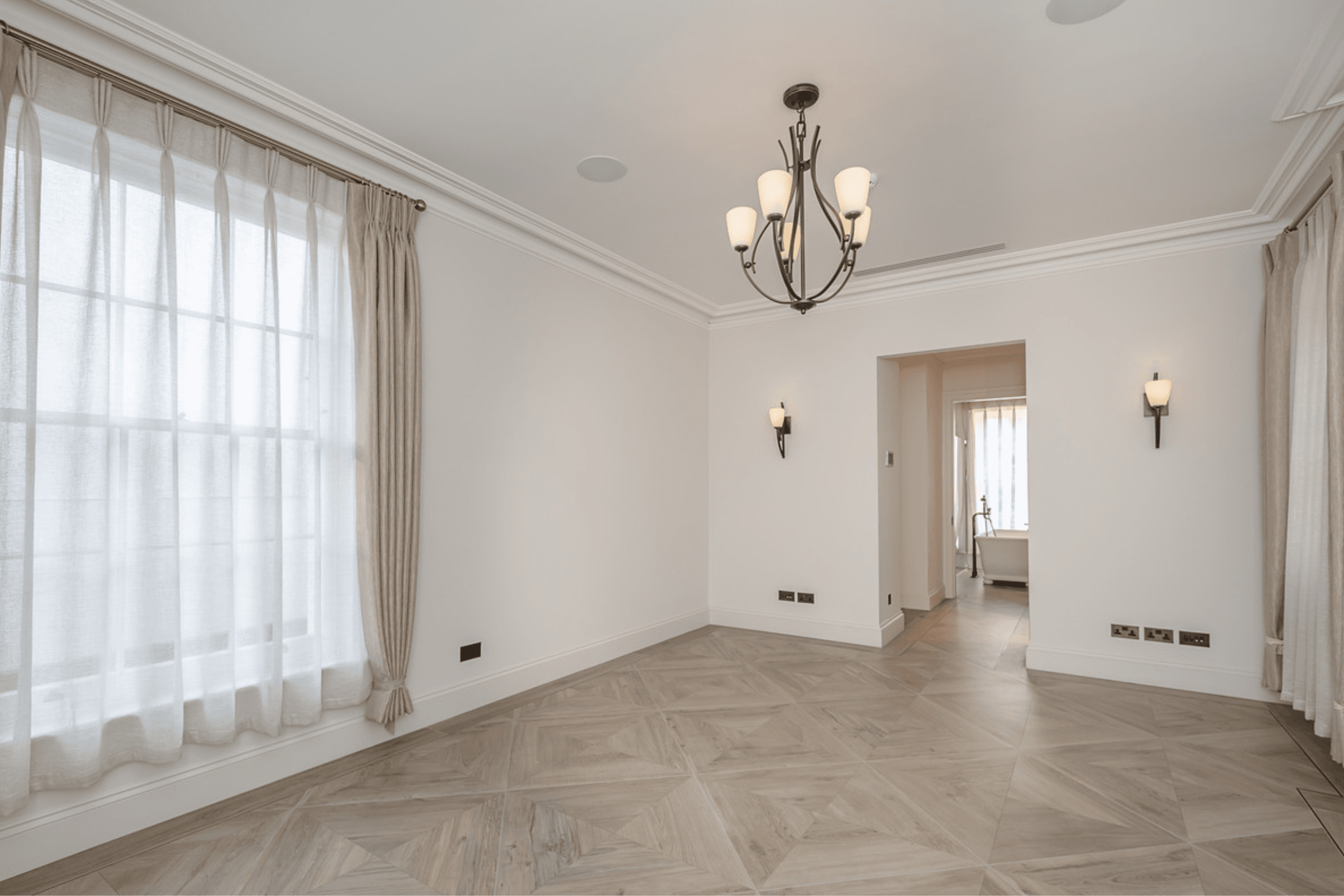 Spacious reception room with high ceilings, herringbone parquet flooring, chandelier lighting and fireplace overlooking the street.
