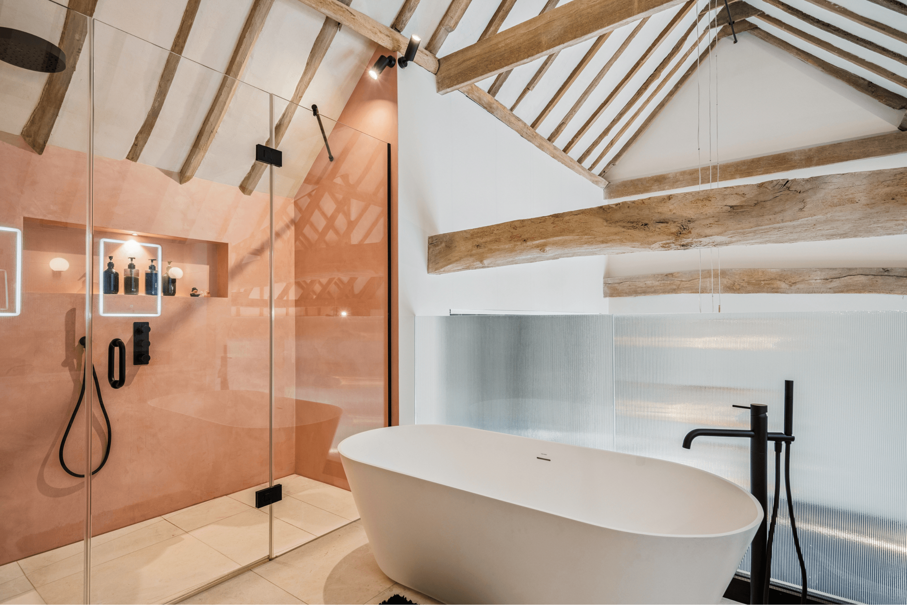 Bathroom with freestanding bath, walk-in shower and exposed timber beams beneath the vaulted barn roof.