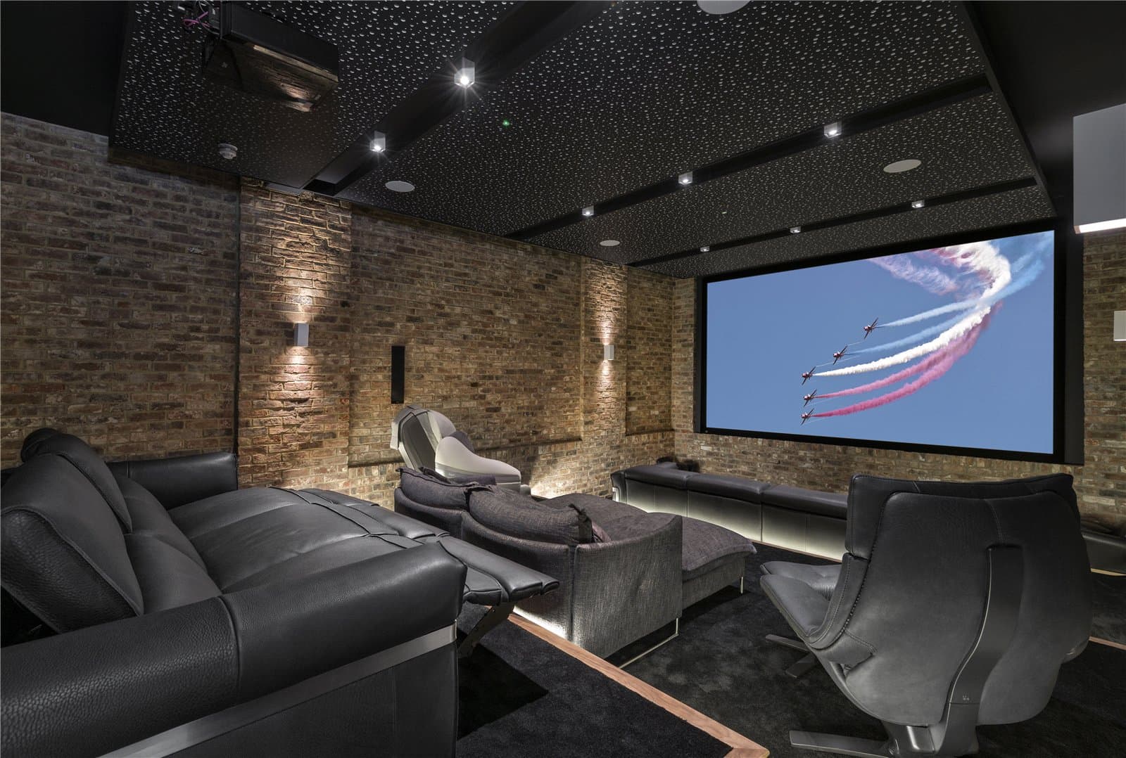 A cinema room with exposed brick walls, a starlit style ceiling with recessed lighting, black leather reclining seating arranged in two rows, and a large wall mounted screen. The Warren, Radlett, Hertfordshire, listed with Prime Property.
